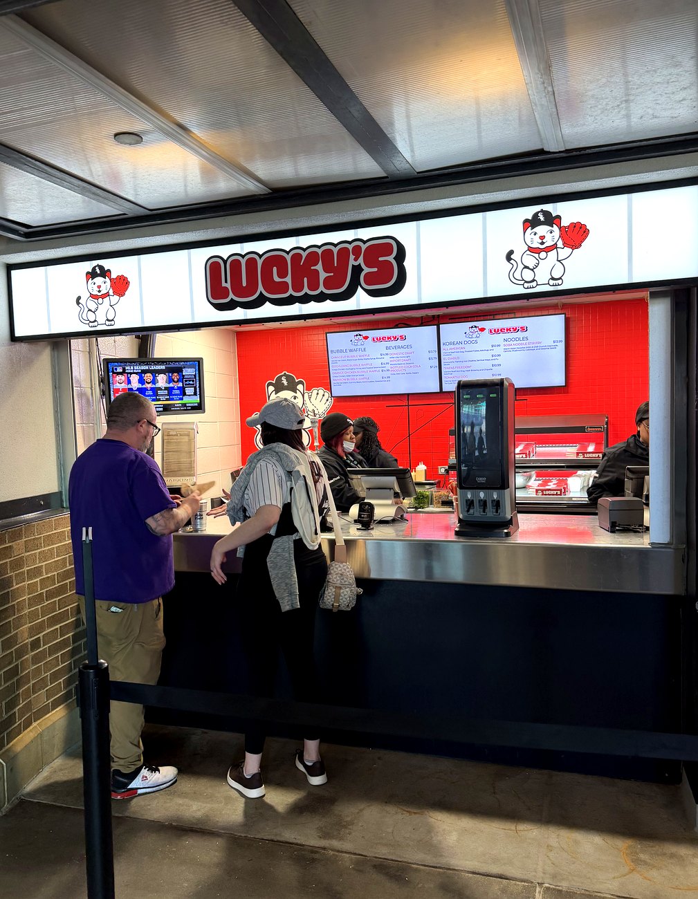 The Lucky's concession stand at Rate Field, with the red Lucky's sign and menu boards above the counter and fans ordering